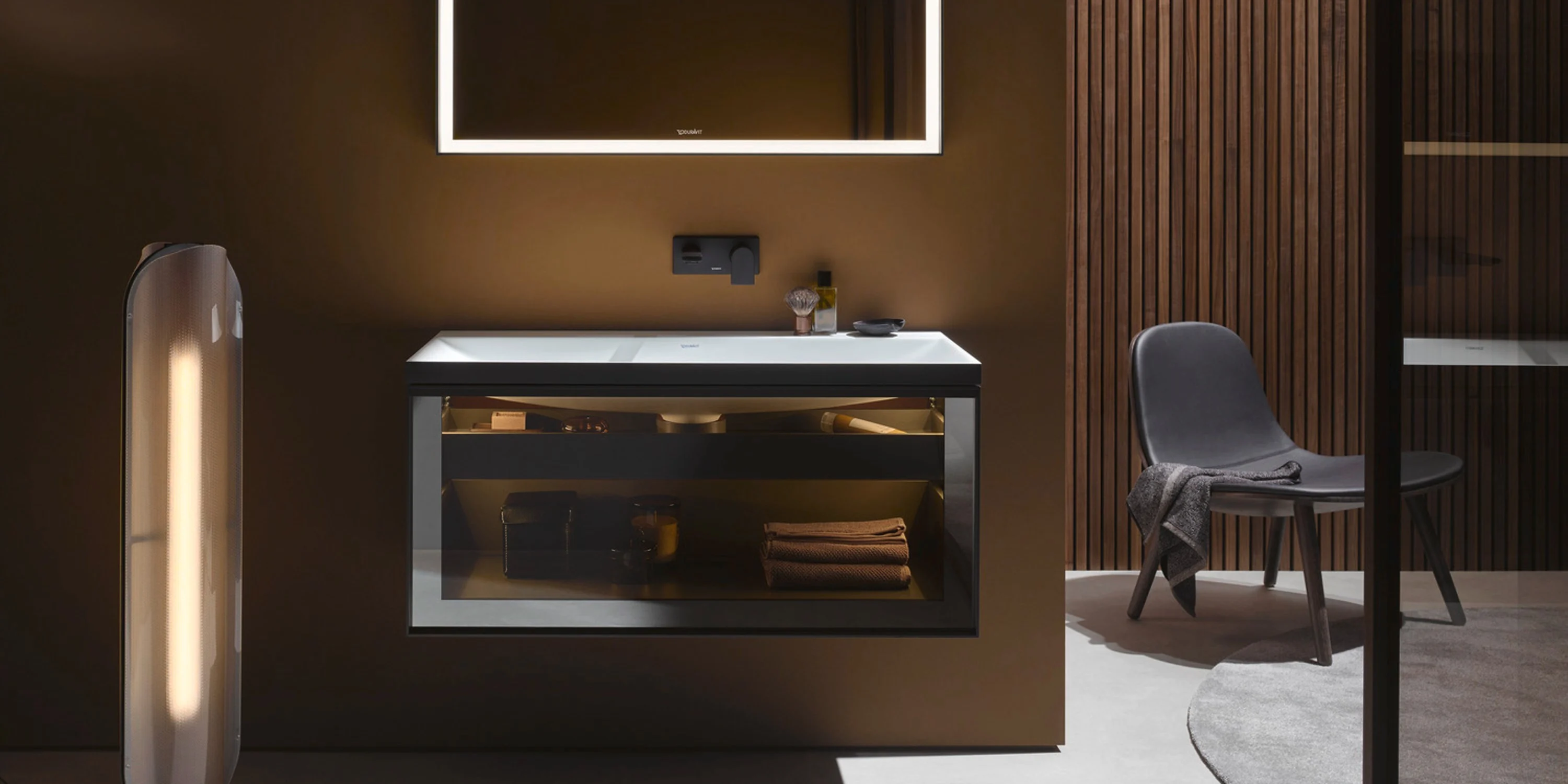 Dark walnut vanity with an illuminated mirror in a warm bronze bathroom